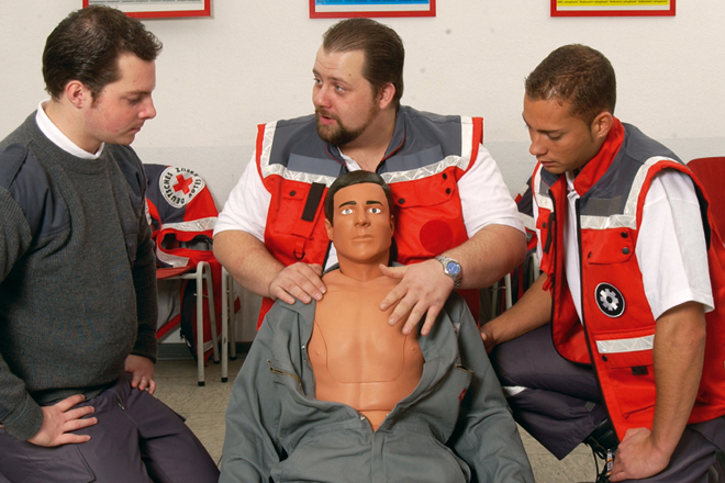 Im Rahmen einer Erste Hilfe Fortbildung erhält ein betrieblicher Ersthelfende Informationen zur Herzdruckmassage von zwei Ausbildern des DRK.