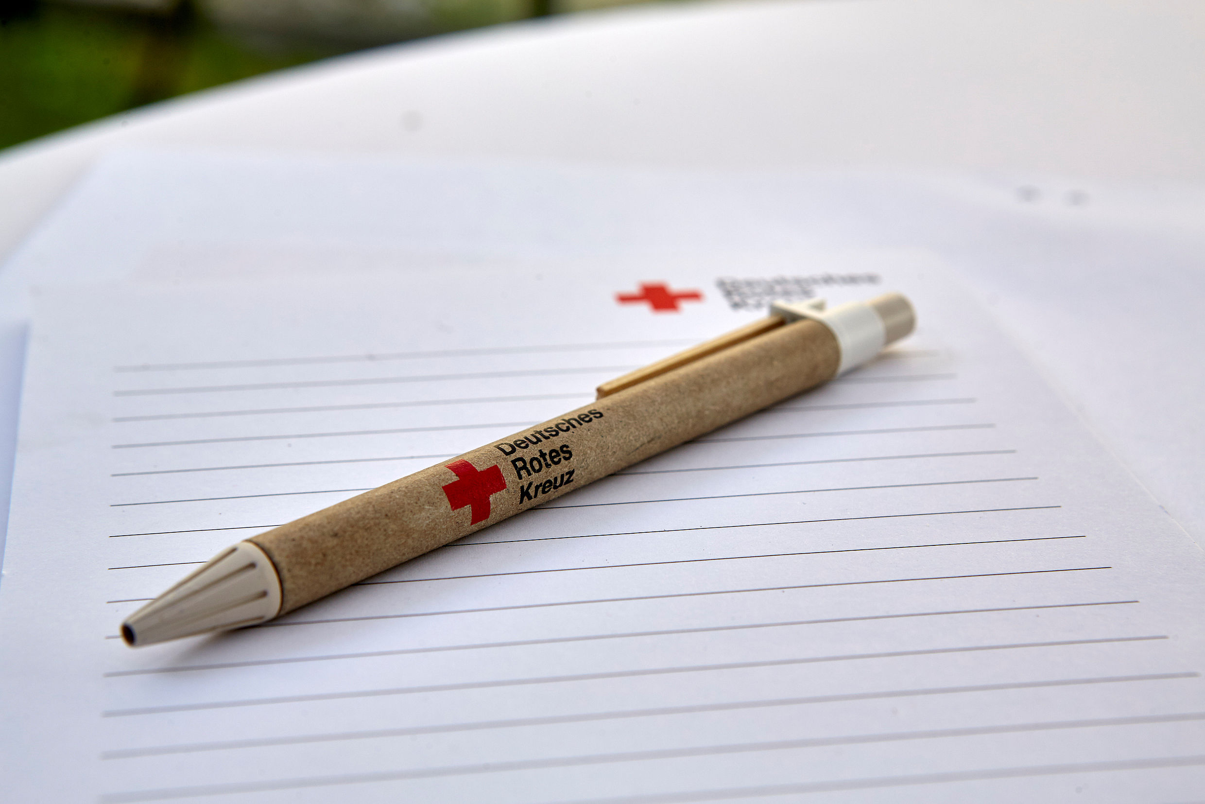 Stift und Schreibblock mit DRK-Logo liegen auf einem Stehtisch.