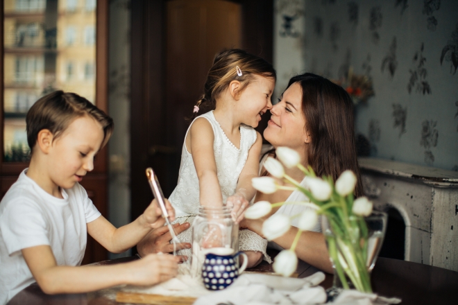Eine Mutter ist gemeinsam mit ihrer Tochter und ihrem Sohn an einem Tisch zu sehen. Die Mutter ist in Verbindung mit ihrer Tochter. 