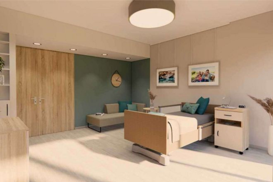 Blick in ein Pflegezimmer. Das Bett steht an der rechten Wand. Ins Blick fällt die Breite Eingangstür und das Sofa für Zugehörige.