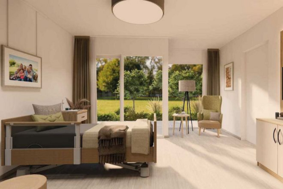Blick in ein Pflegezimmer. Das Bett steht an der linken Wand. Der Blick geradeaus fällt auf die Fensterfront und die sich daran anschließende Terrasse. 