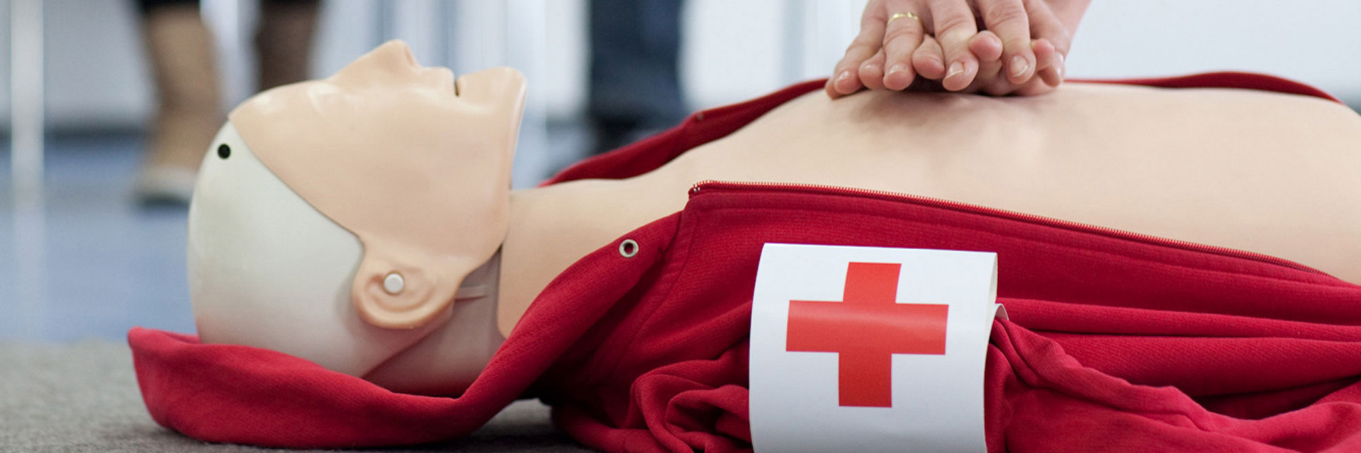 Bei einem Erste Hilfe Kurs liegt eine Dummy-Puppe am Boden, an der gerade die Herzdruckmassage geübt wird. 
