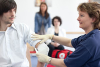 Kursleitung legt einen Verband am Arm eines jungen Mannes an.