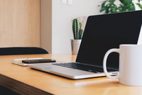 Schreibtisch mit aufgeklapptem Laptop, Tasse, Block und Stift