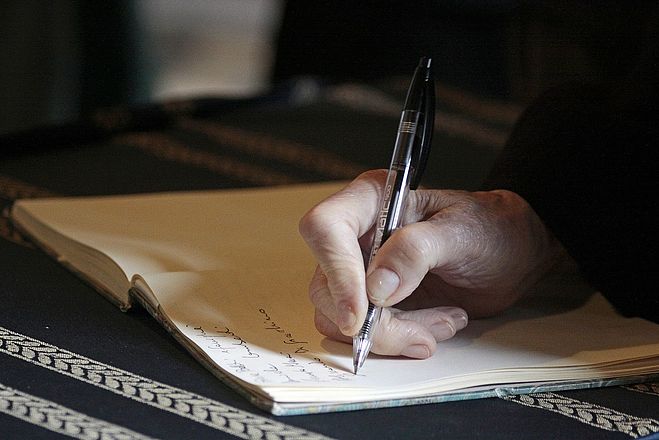 Person hält einen Stift in der Hand und schreibt in ein Buch. 
