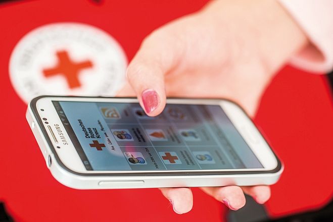 Smartphone in der Hand und Startbildschirm der DRK-App ist sichtbar.